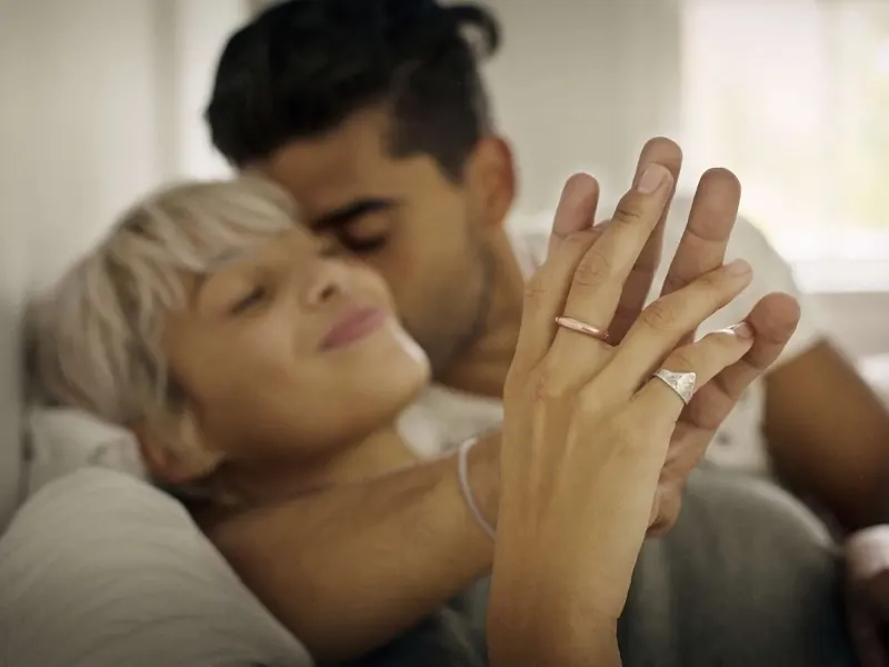 A smiling couple lying close together in bed, holding hands (brand stock photo, models)